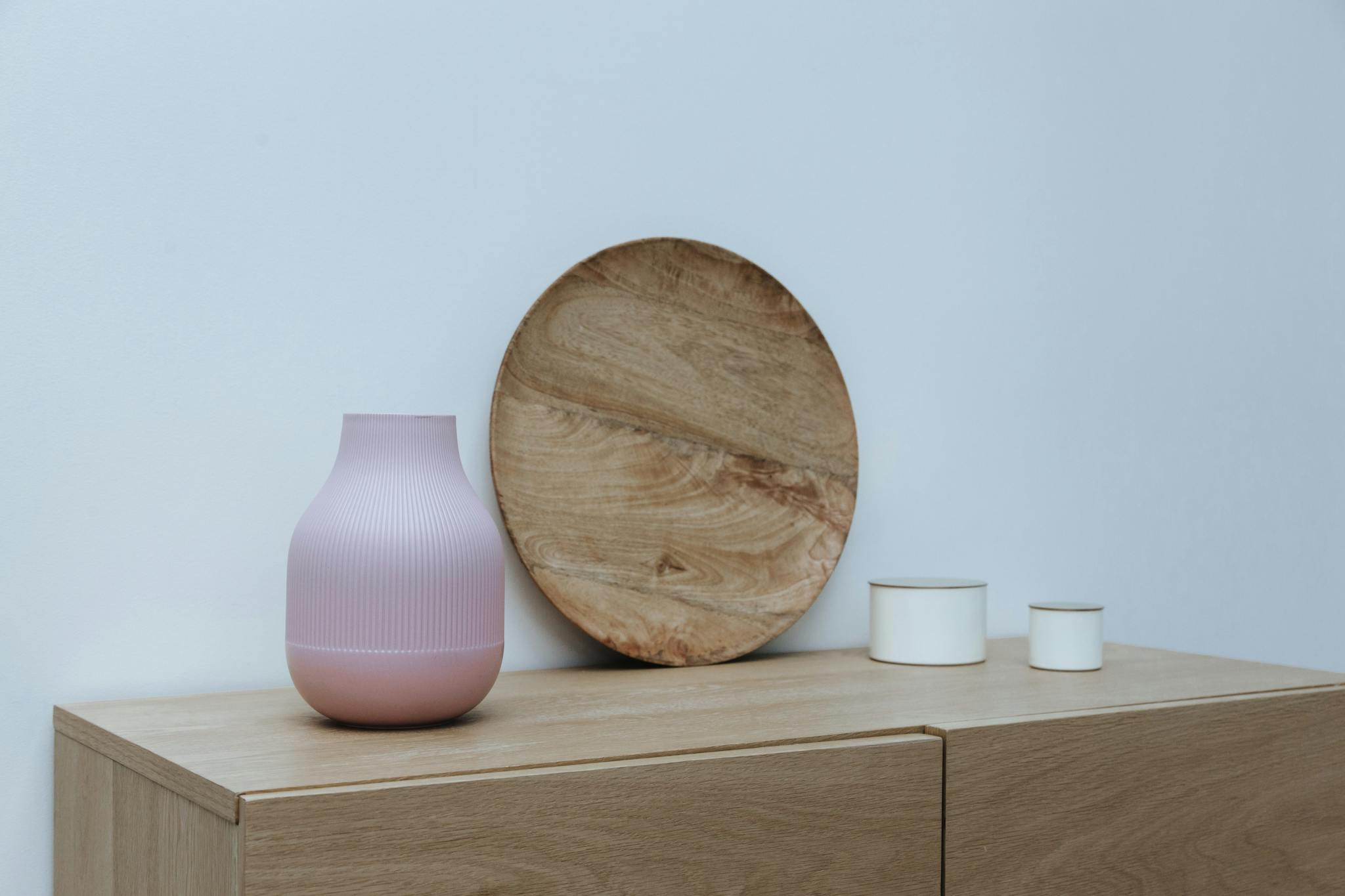 Stylish minimalist interior setup featuring wooden decor and a pink vase on light wooden furniture.